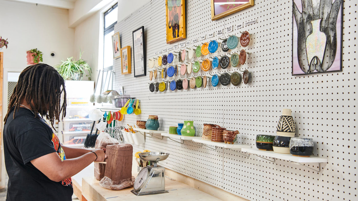 Person working in a pottery studio with shelves of ceramic items and wall art.