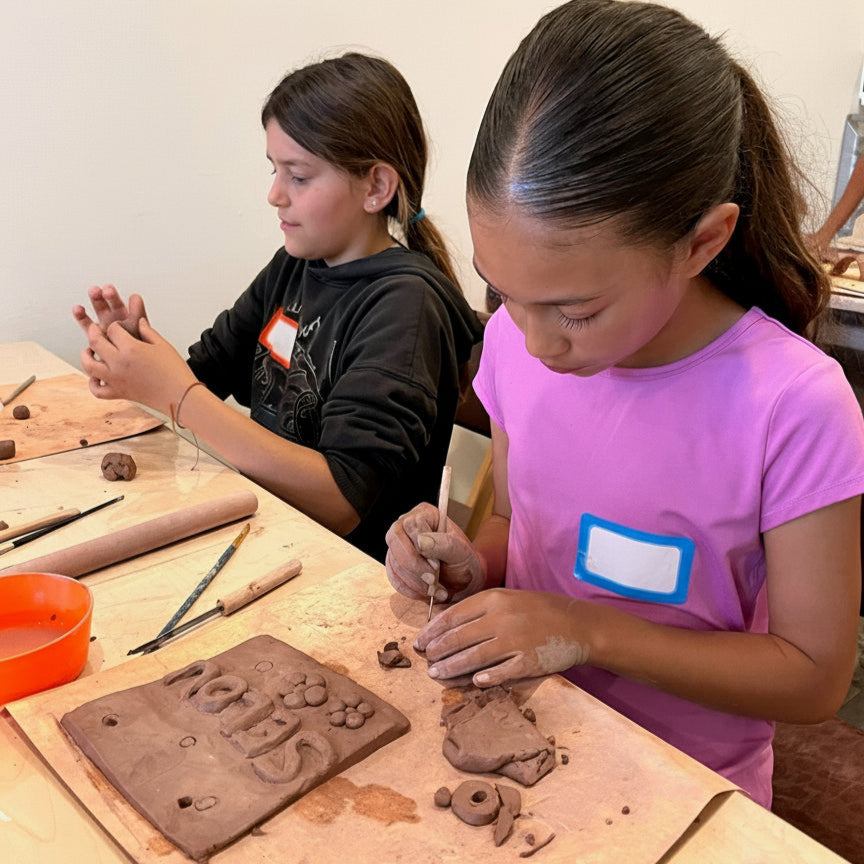 Two children working with clay at a table, wearing name tags.